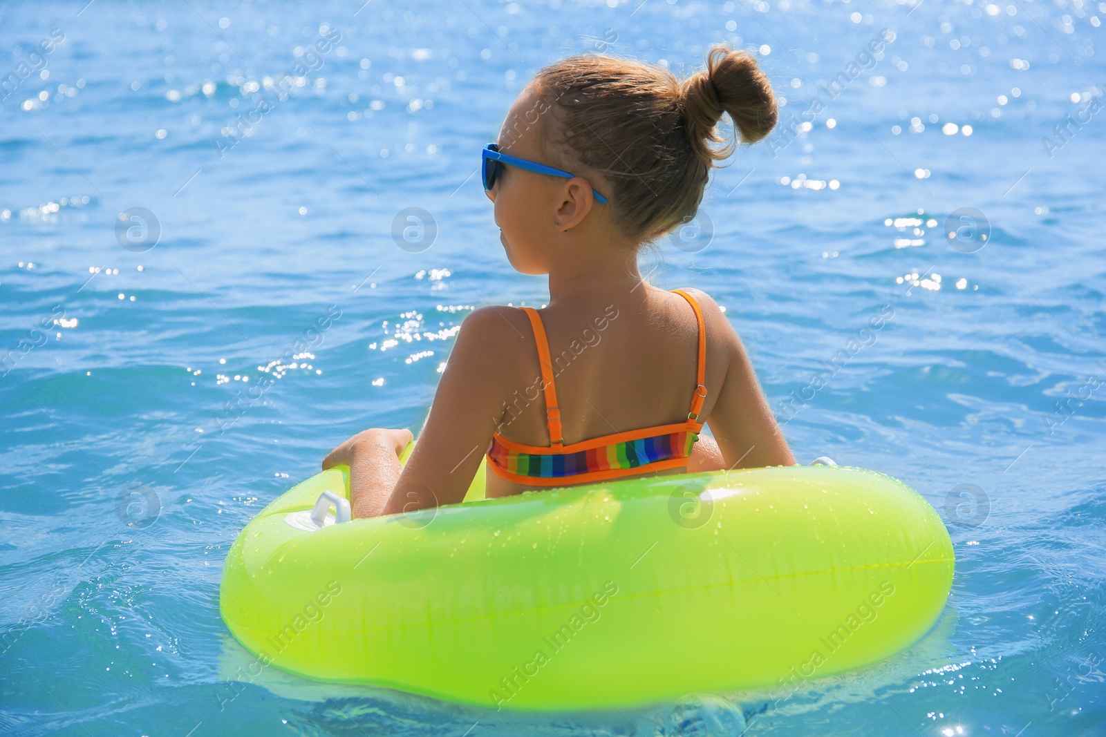 Photo of Little girl with sunglasses and inflatable ring in sea on sunny day. Beach holiday