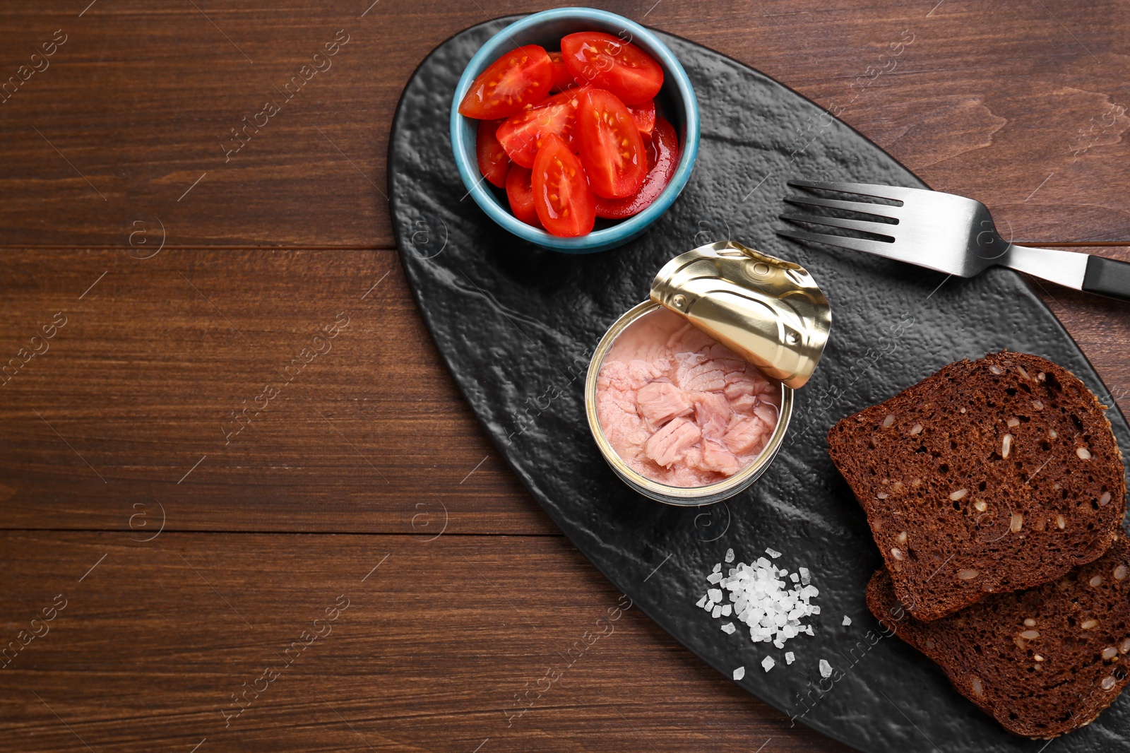 Photo of Can of conserved tuna, tomatoes and bread on wooden table, top view. Space for text