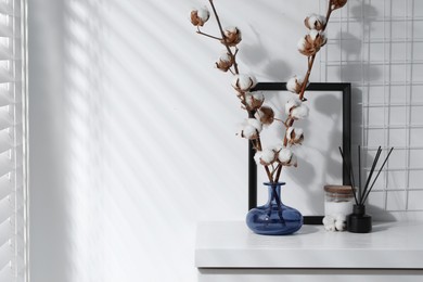 Photo of Reed diffuser, candle and cotton branches with fluffy flowers on white wooden table indoors. Space for text