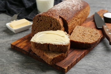 Photo of Tasty freshly baked bread with butter on grey table