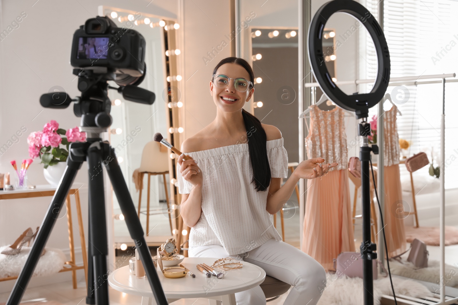 Photo of Blogger with brush recording video in dressing room at home. Using ring lamp and camera