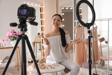 Photo of Blogger with brush recording video in dressing room at home. Using ring lamp and camera