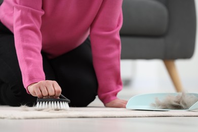 Photo of Woman with brush removing pet hair from carpet at home, closeup