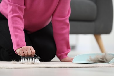 Woman with brush removing pet hair from carpet at home, closeup