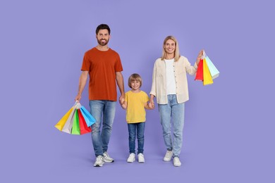 Family shopping. Happy parents and son with many colorful bags on violet background