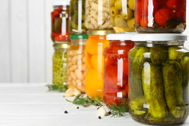 Glass jars with different pickled foods on white wooden background, closeup