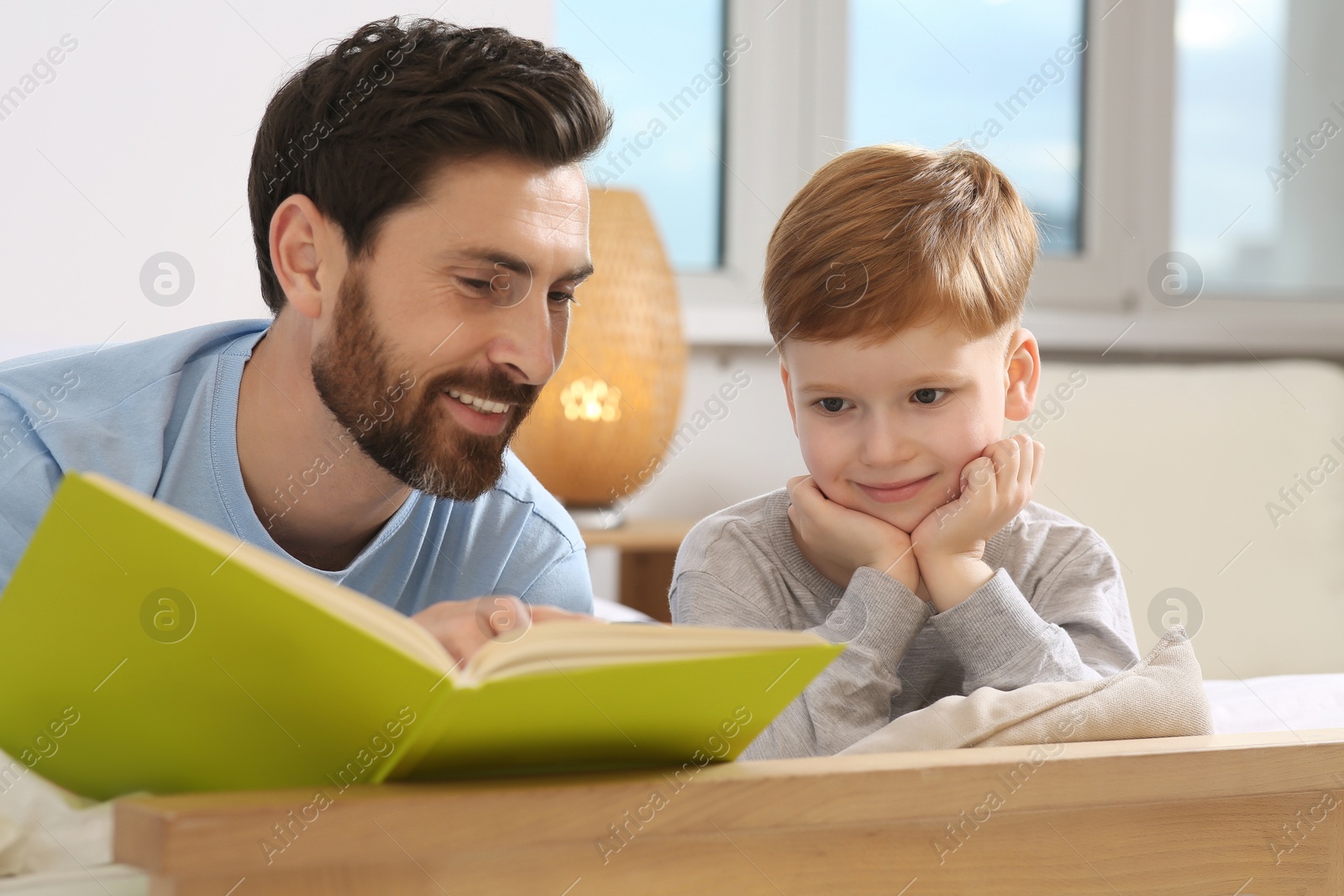 Photo of Father reading book with his child on bed at home