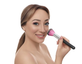 Beautiful young woman applying face powder with brush on white background