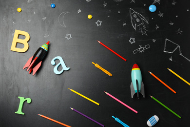 Photo of Bright toy rockets, school supplies and drawings on chalkboard, flat lay