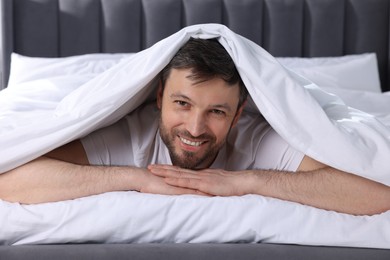 Happy man wrapped in blanket on soft bed