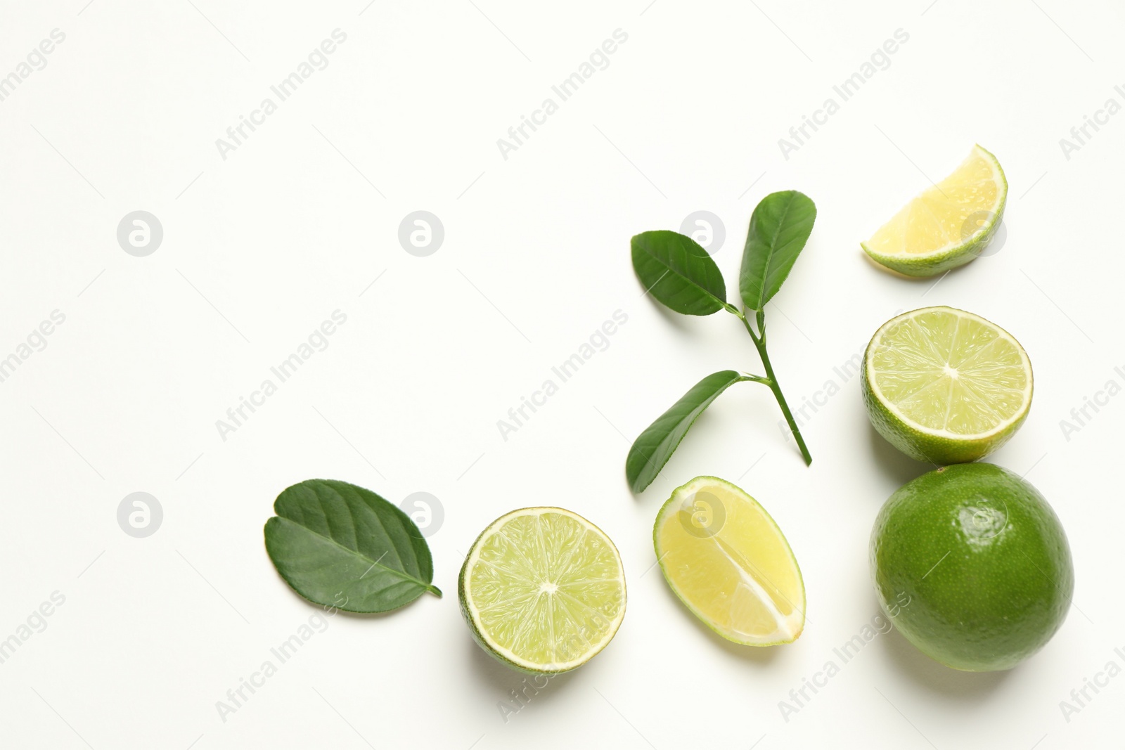 Photo of Whole and cut fresh ripe limes with green leaves on white background, flat lay