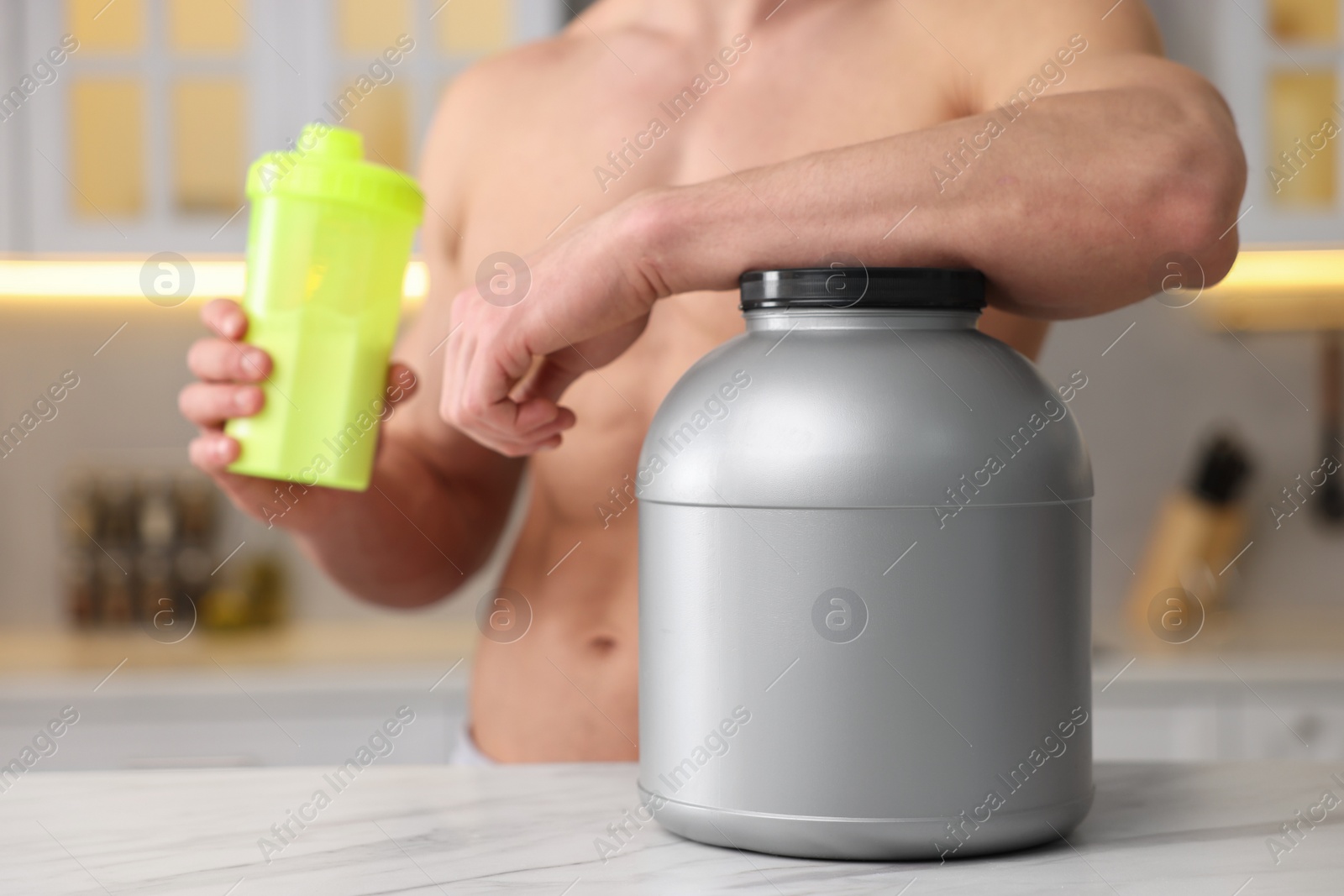 Photo of Young man with shaker of protein and powder at white marble table in kitchen, closeup