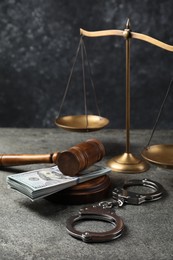 Photo of Judge's gavel, money, handcuffs and scales of justice on grey table
