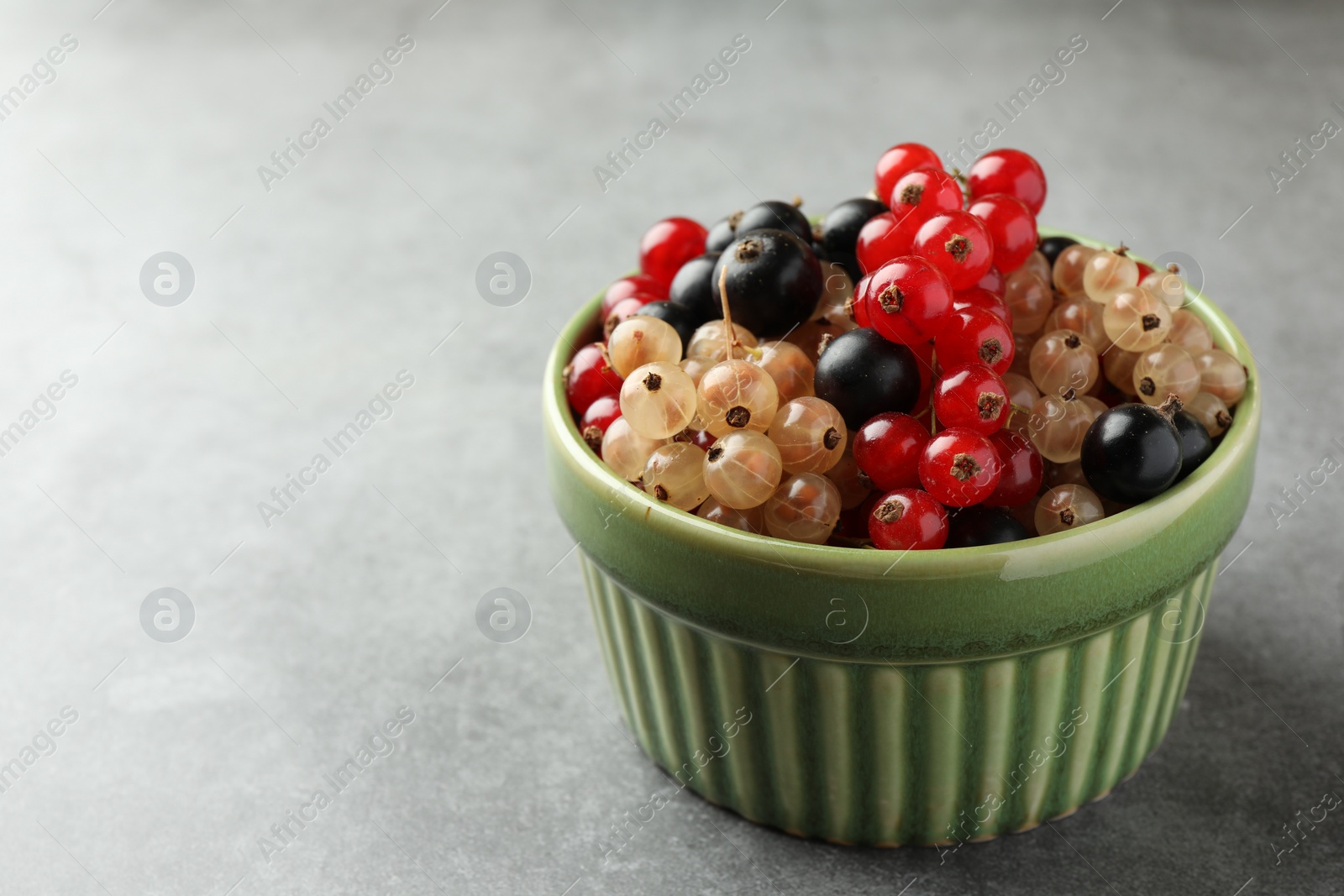 Photo of Different fresh ripe currants in bowl on light grey table, closeup. Space for text
