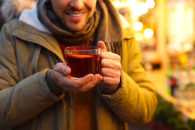 Happy man with mulled wine at winter fair, closeup