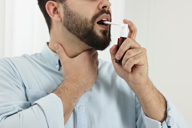 Photo of Young man using throat spray indoors, closeup