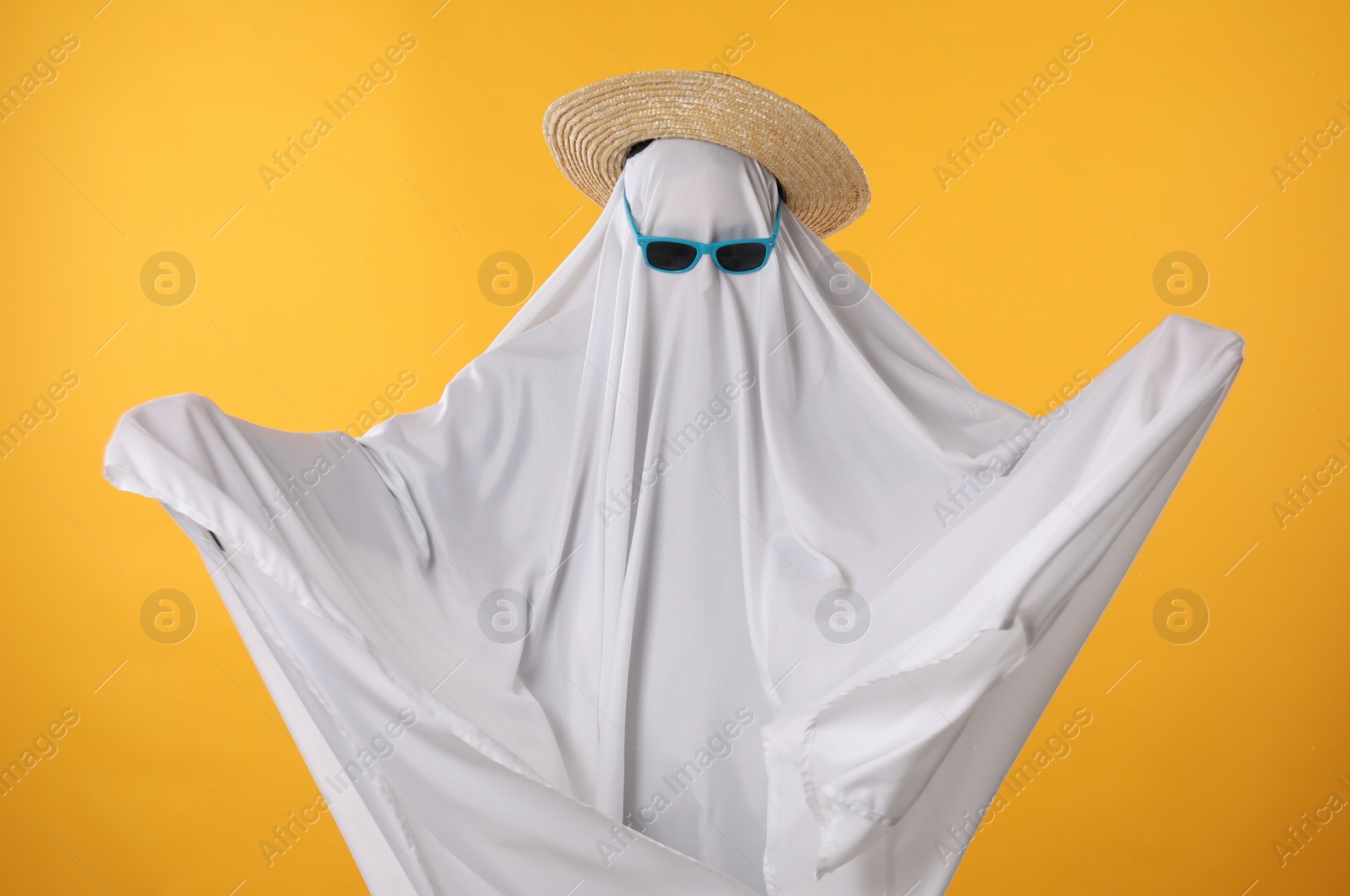 Photo of Person in ghost costume, sunglasses and straw hat on yellow background