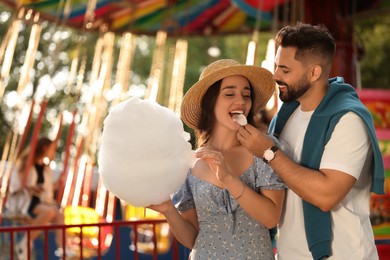 Photo of Young man feeding his girlfriend with cotton candy at funfair