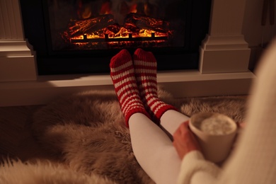 Woman in warm socks resting near fireplace with burning woods indoors, closeup