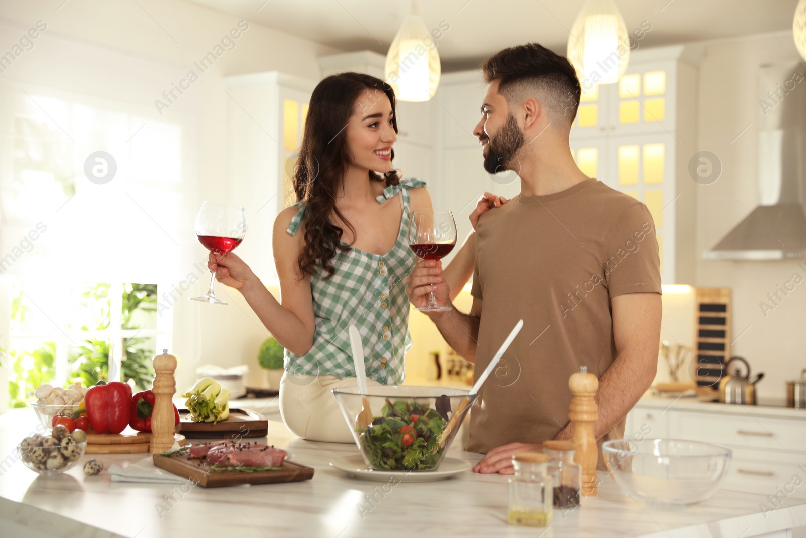 Photo of Lovely young couple drinking wine while cooking together at kitchen