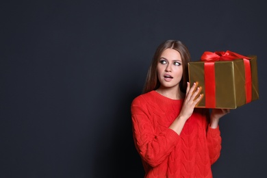 Photo of Emotional young woman with Christmas gift on dark background. Space for text