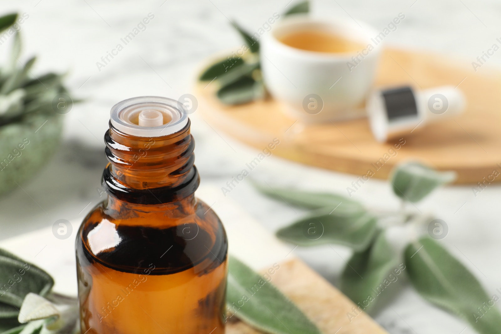 Photo of Bottle of essential sage oil and leaves on table, closeup. Space for text