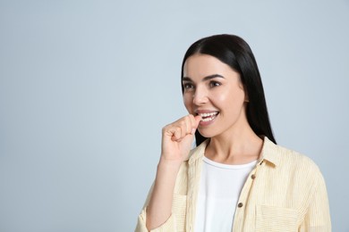 Photo of Young woman biting her nails on light grey background. Space for text