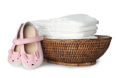 Photo of Wicker bowl with disposable diapers and child's shoes on white background