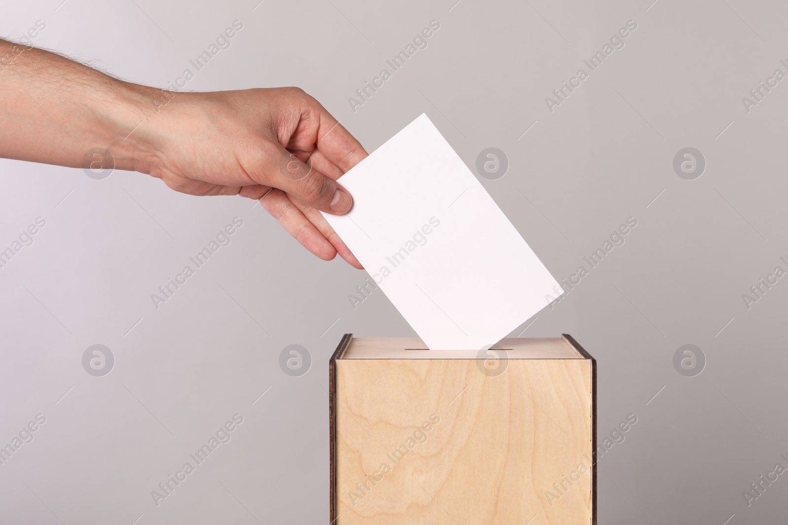 Photo of Man putting his vote into ballot box on light grey background, closeup