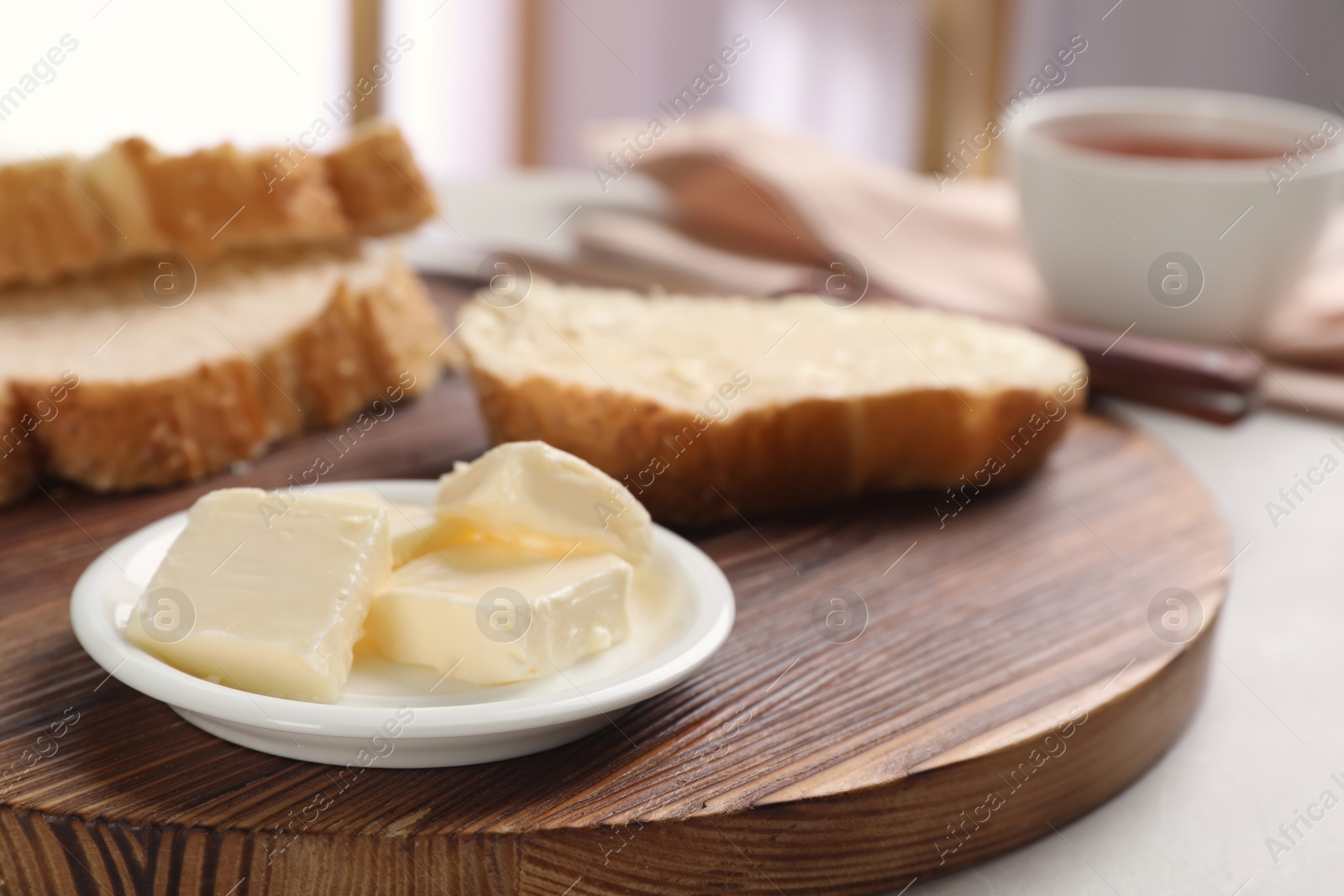 Photo of Plate with tasty butter and fresh bread on wooden board