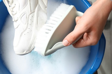 Woman cleaning stylish sneakers with brush in wash basin, top view