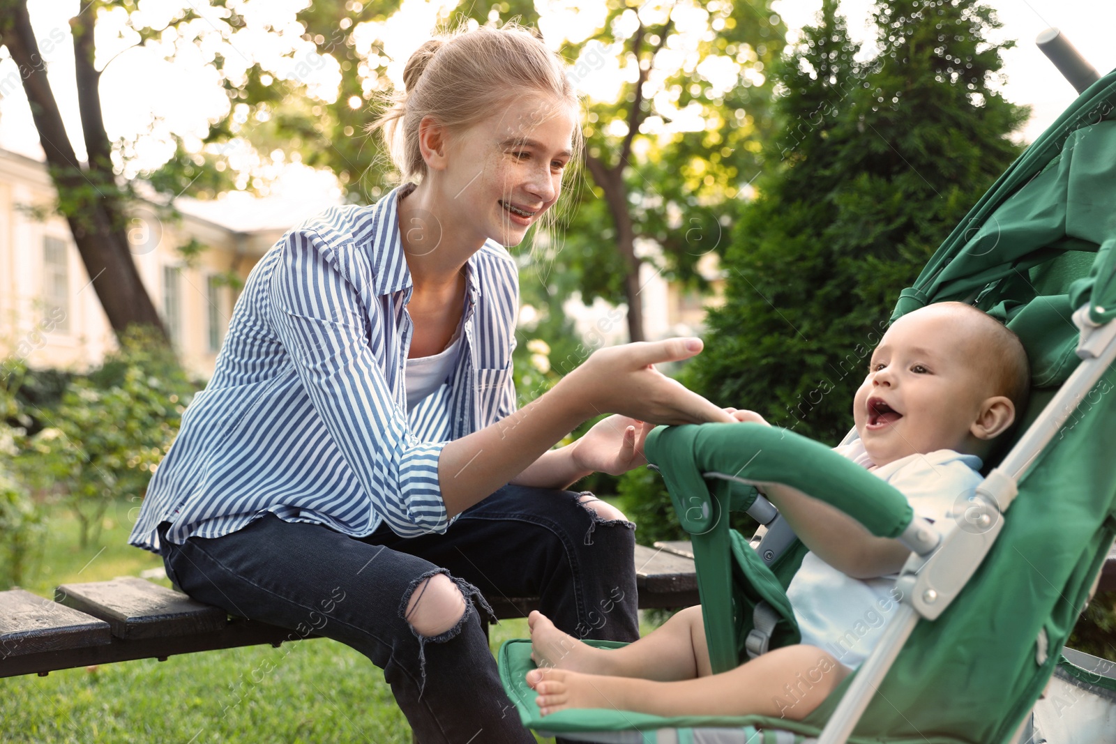 Photo of Teen nanny with cute baby in stroller playing in park