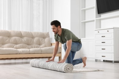 Smiling man unrolling carpet with beautiful pattern on floor in room