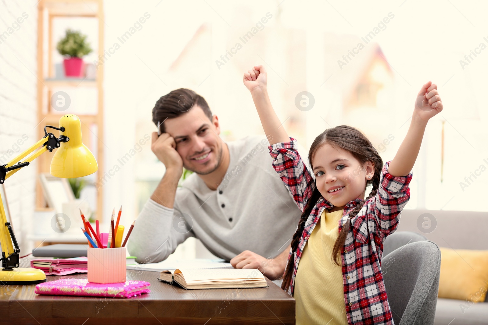 Photo of Father and daughter doing homework together at table indoors