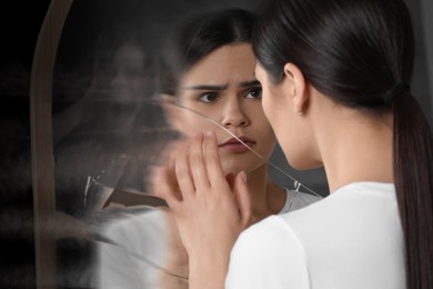 Image of Suffering from hallucinations. Woman seeing her reflection screaming in broken mirror