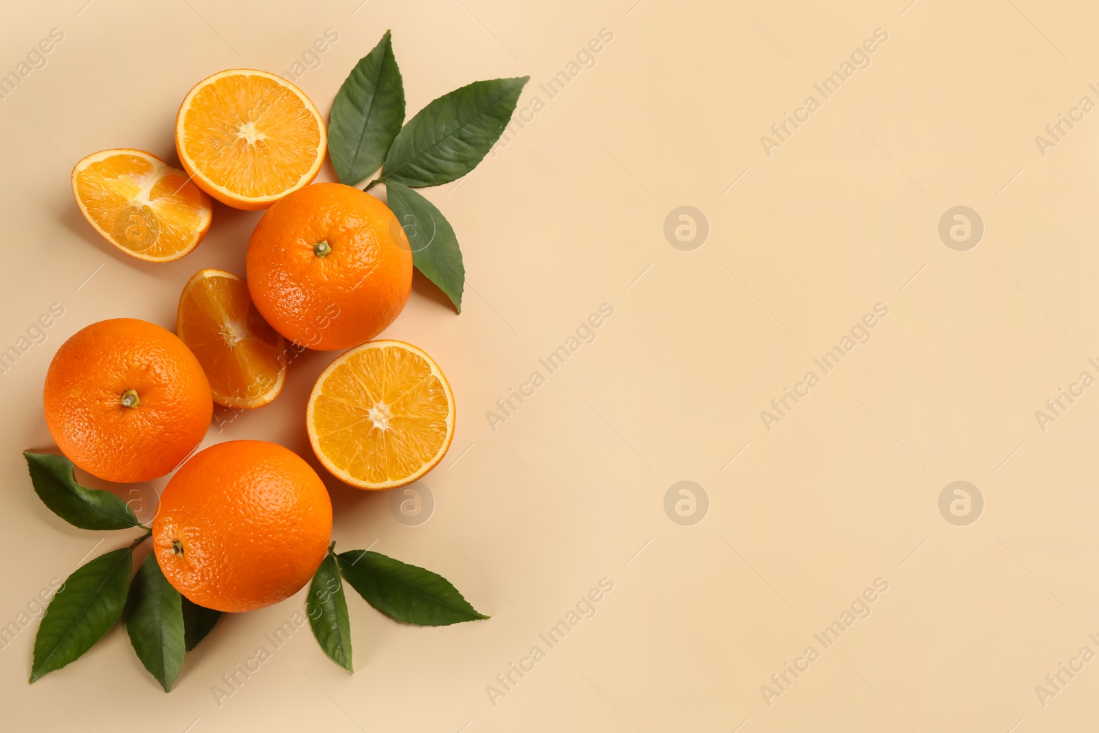 Photo of Fresh ripe oranges with green leaves on beige background, flat lay. Space for text