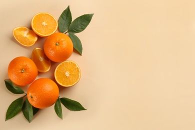 Fresh ripe oranges with green leaves on beige background, flat lay. Space for text