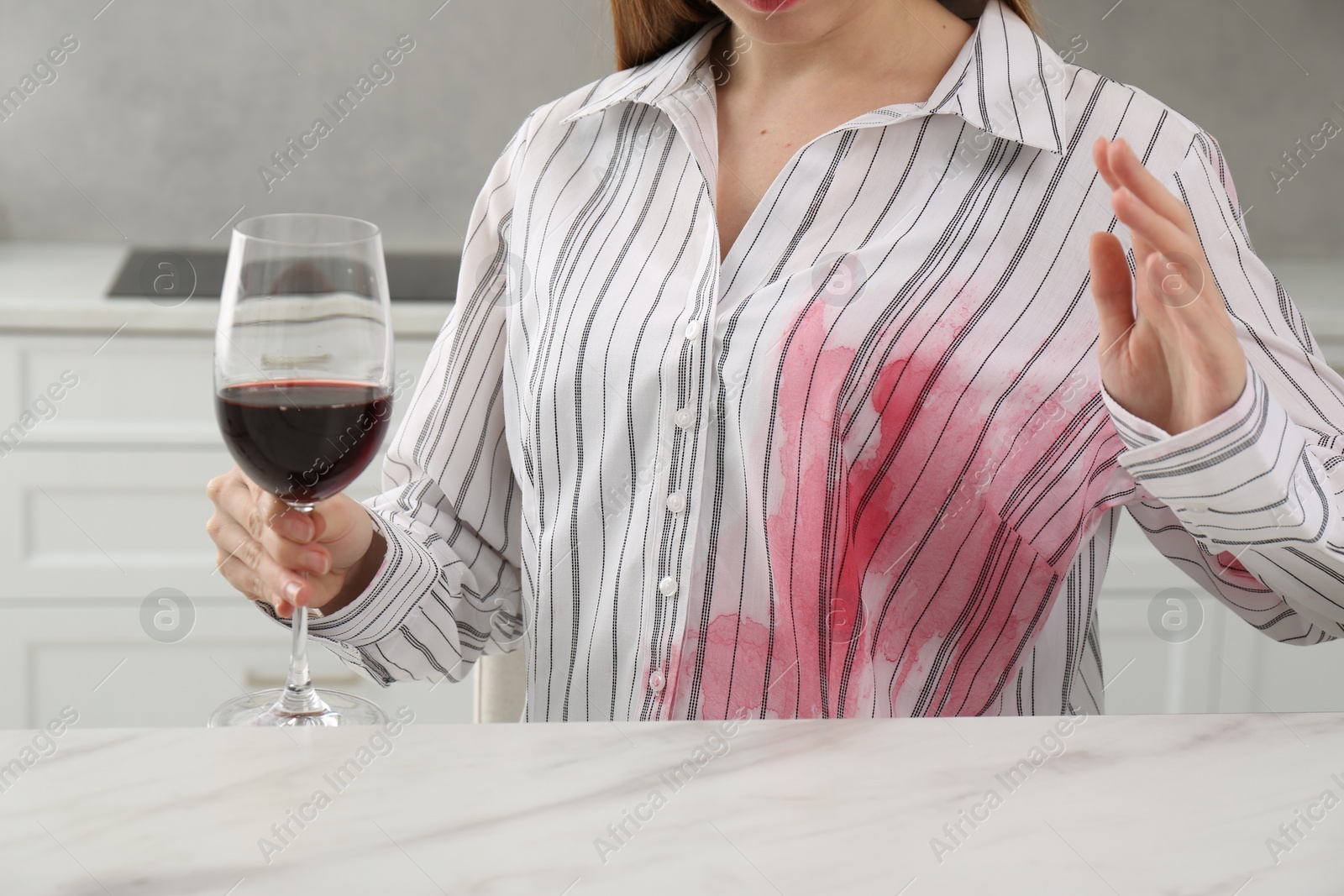 Photo of Woman with spilled wine over her shirt at marble table indoors, closeup