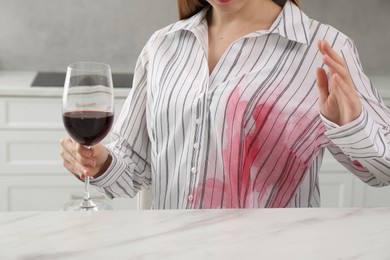 Woman with spilled wine over her shirt at marble table indoors, closeup