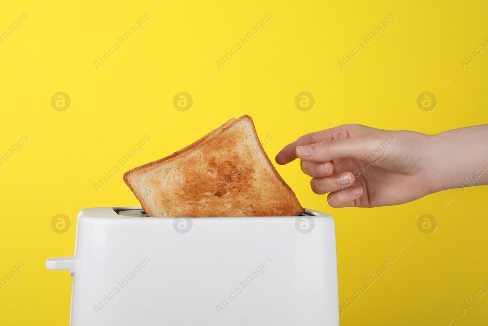 Photo of Woman taking slice of bread from white toaster on yellow background, closeup