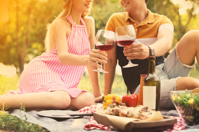 Image of Happy couple with glasses of wine sitting on lawn, closeup. Summer picnic