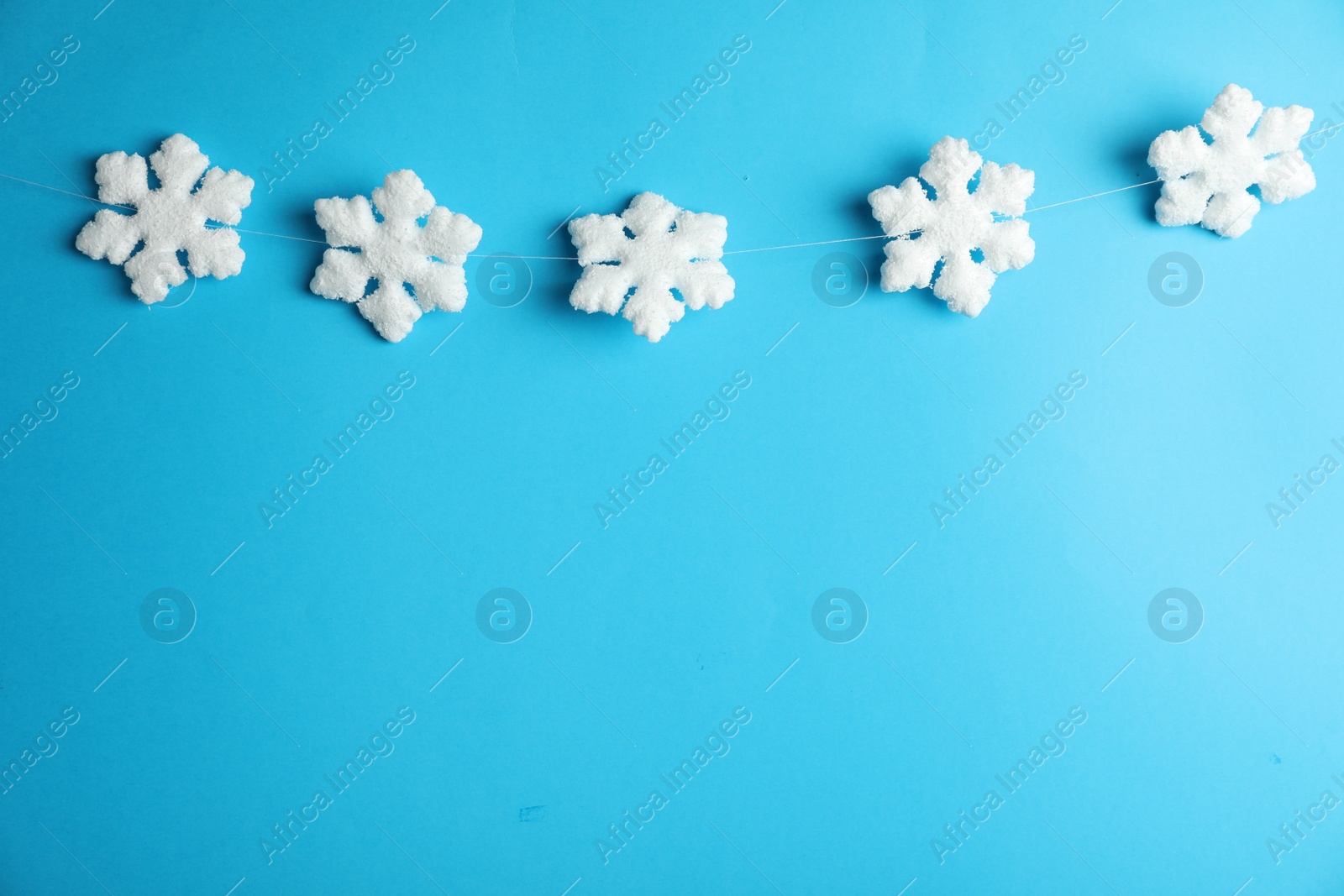 Photo of Beautiful decorative snowflakes hanging on light blue background, space for text