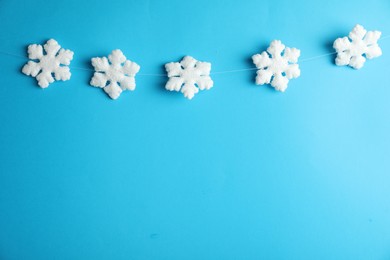 Photo of Beautiful decorative snowflakes hanging on light blue background, space for text