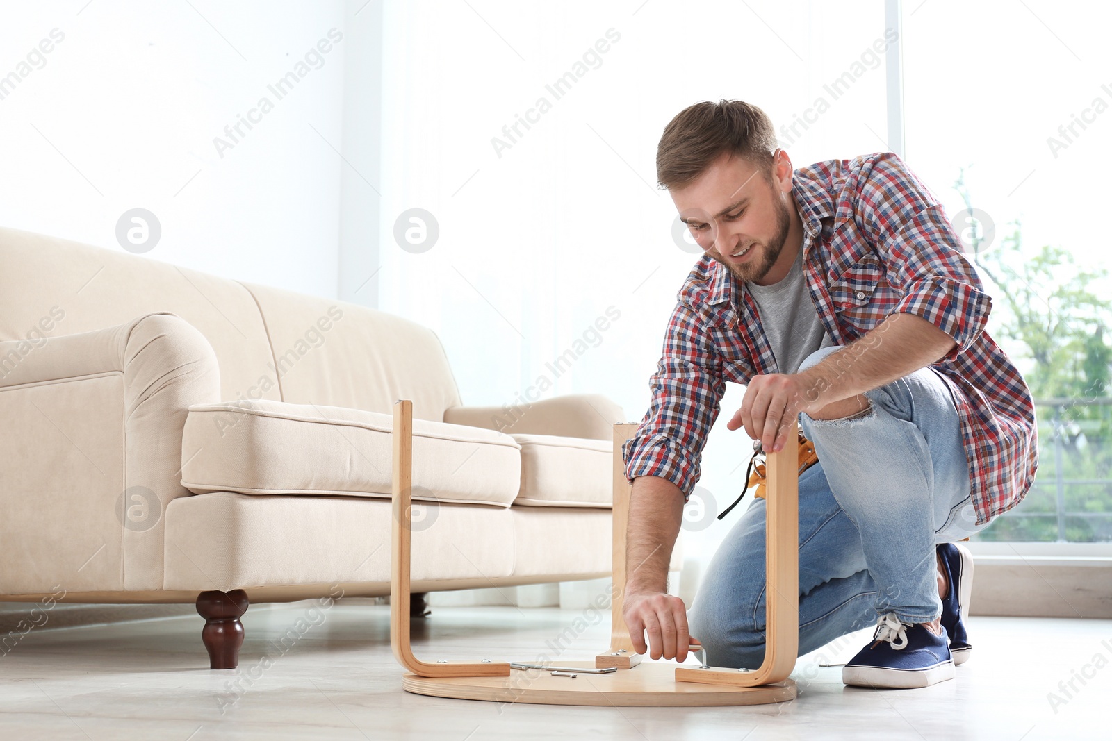 Photo of Young man working with wooden chair indoors. Space for text