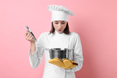 Professional chef with cooking pot on pink background