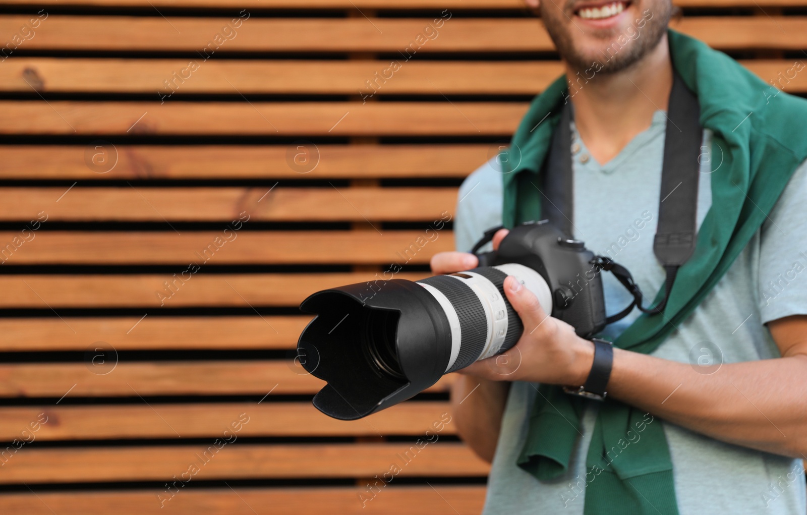 Photo of Young male photographer with professional camera near wooden wall. Space for text