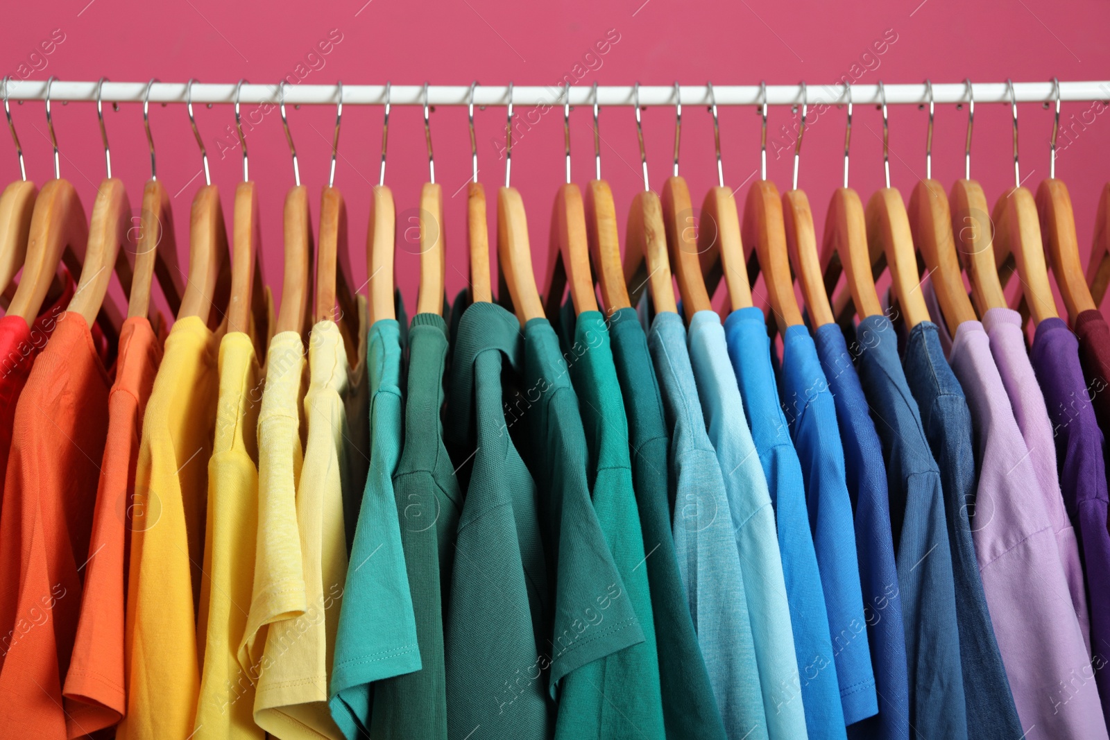 Photo of Rack with bright clothes on pink background. Rainbow colors