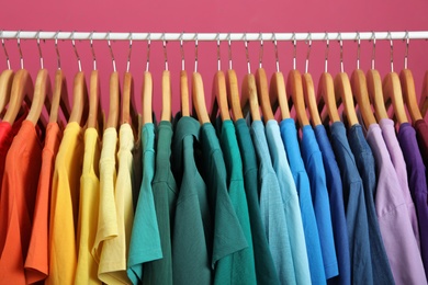 Photo of Rack with bright clothes on pink background. Rainbow colors