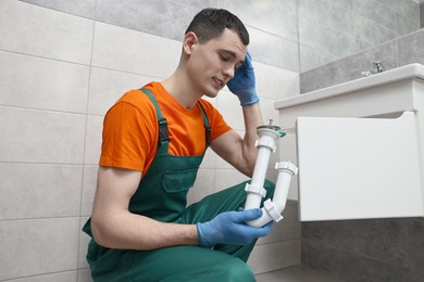 Photo of Thoughtful plumber wearing protective gloves repairing sink in bathroom