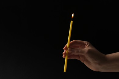 Photo of Woman holding burning church candle on black background, closeup